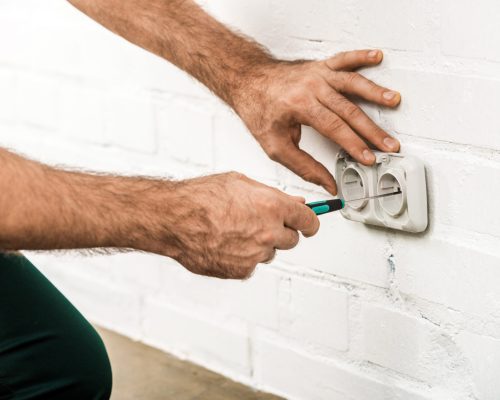 cropped image of electrician repairing power socket with screwdriver at home