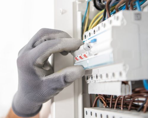 Electrician Wearing Safety Gloves Testing Fuses Inside an Apartment Located Electric Box.